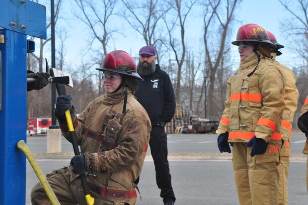 A high school student uses a firefighter's axe to assist in forcing a door open