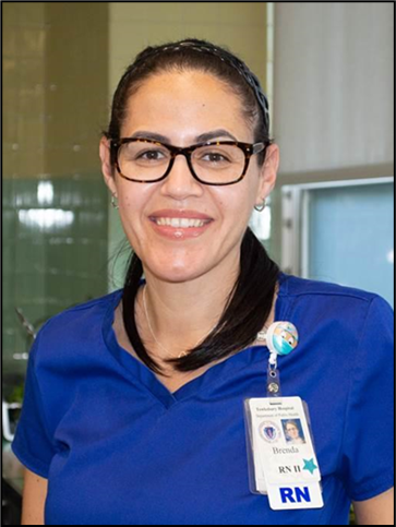 Brenda Baez is a registered nurse. She wears her hair in a ponytail. She wears black glasses. She is wearing a blue medical uniform with her name badge pinned on the front. She looks very friendly with a welcoming smile in this photo.