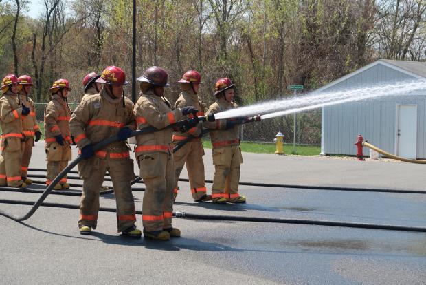 Firefighters help high school students use a firehose