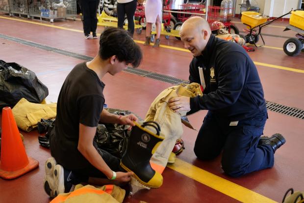 Firefighter assists high school student with turnout gear