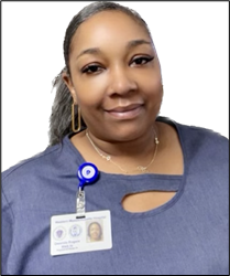 Qwanda is a registered nurse. She has sleek, dark long hair in a ponytail. She is wearing a blue top with her name badge pinned on the front. She looks friendly and has a beautiful smile.