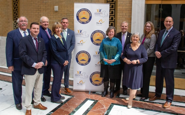A group of legislators stand in front of a banner with the MDDC, Arc and event logos.