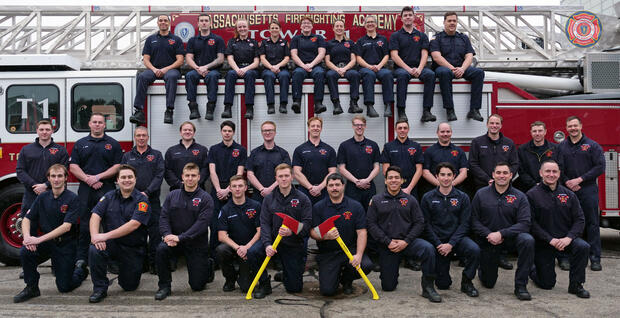 Photo of 32 firefighters on and around a ladder truck