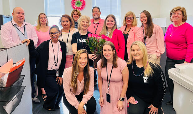 Group of thirteen people in an office dressed in pink