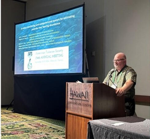 A researcher at a podium presenting his research on a screen.