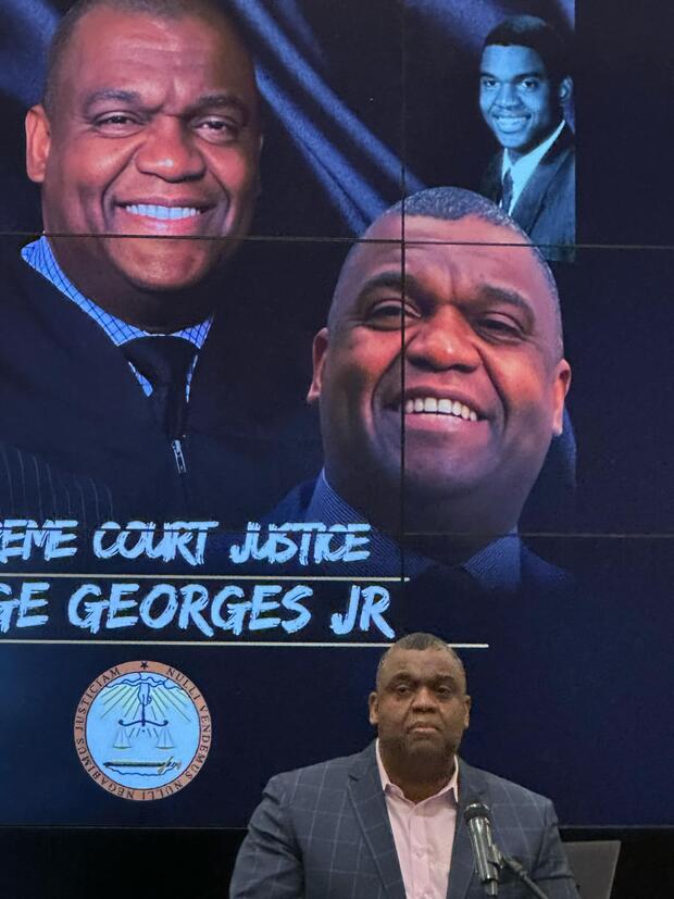 A man stands at a microphone in front of a large screen displaying his images and text.