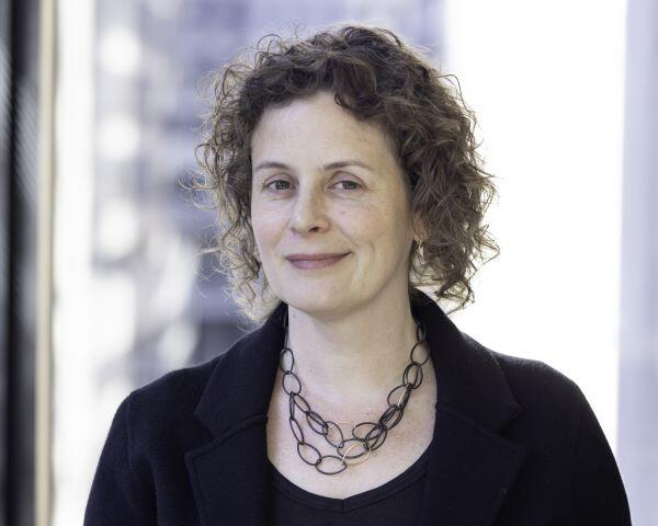 Andrea with curly hair, wearing a necklace and a black top