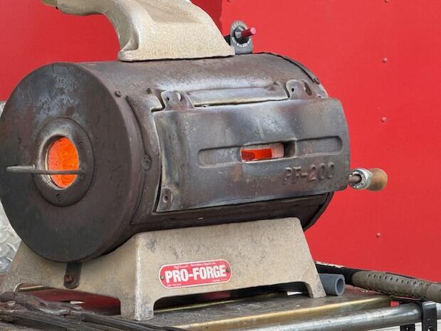 A cylindrical metal forge with a glowing orange interior and a "PRO-FORGE" label.