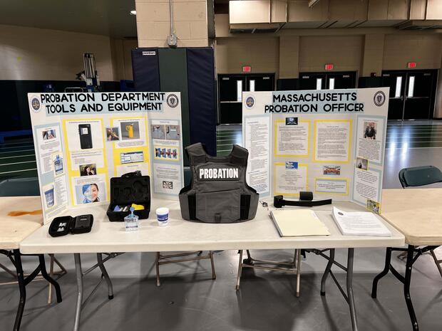 A display on a table showcasing probation department tools and equipment with informative boards and various items, including a "PROBATION" vest.