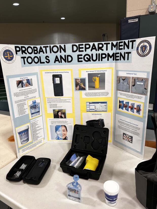 A display board titled "Probation Department Tools and Equipment" showcases probation tools like drug tests and breathalyzers, with samples on a table.