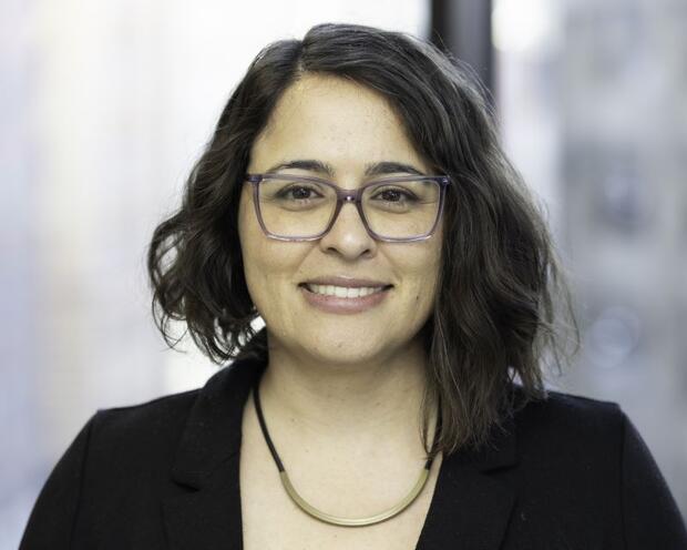Mahsa with glasses, smiling in front of a window, wearing a black top