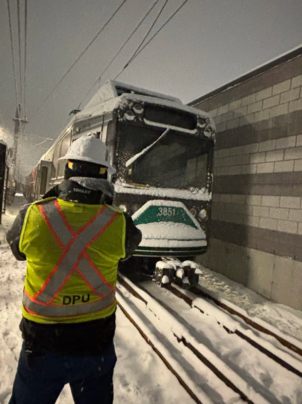 DPU investigator in a yellow and orange vest photographs a train in snowy conditions