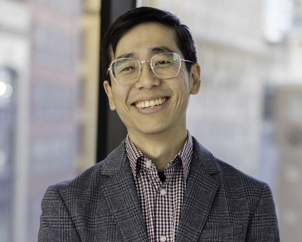 Ta-wei smiling, wearing glasses, a gray suit with checkered pattern, a red shirt with checkered pattern