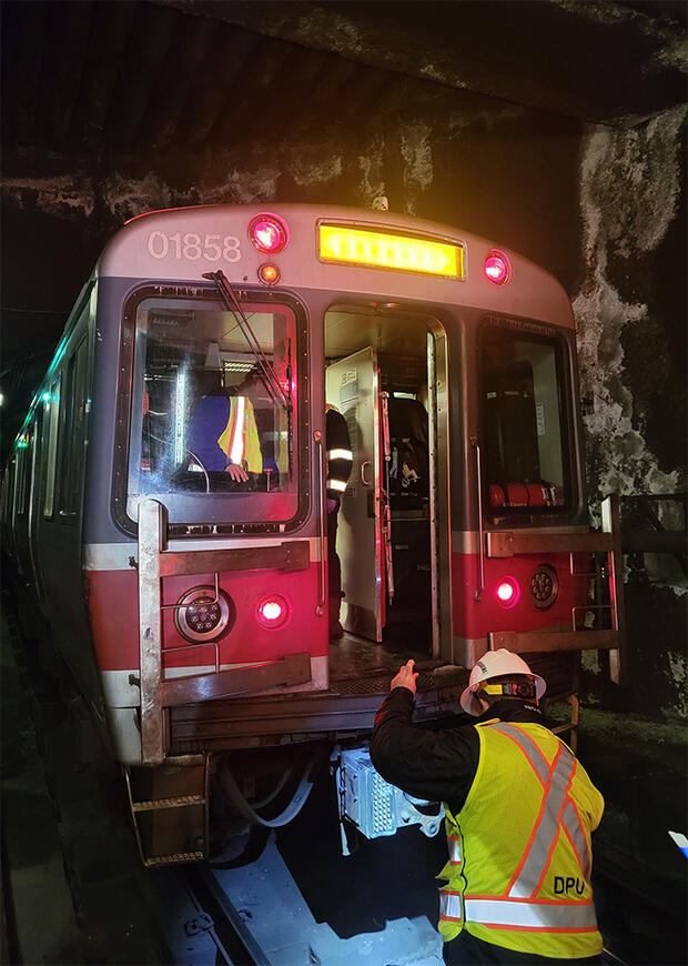 DPU inspector in a yellow and orange vest uses a flashlight to look at track in a dark tunnel