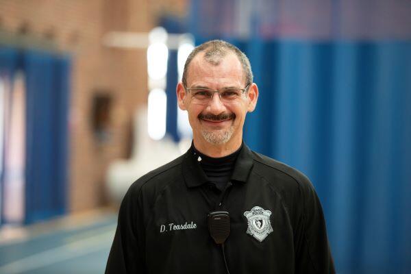 A picture containing person wearing blue security uniform, wearing glasses, face with mustache