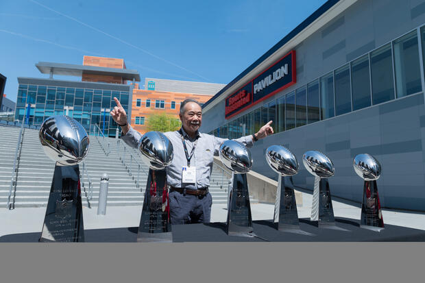 Man poses next to the Super Bowl Trophies. 