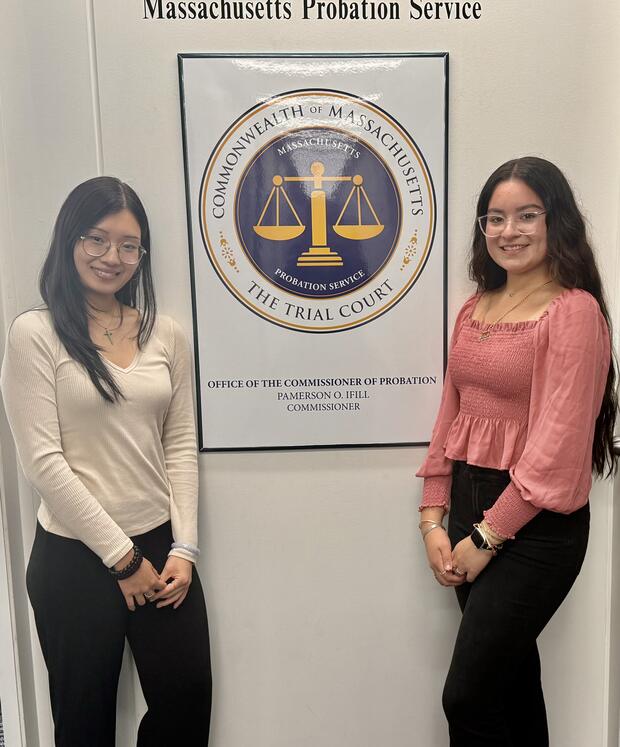 Two individuals standing next to a Massachusetts Probation Service poster featuring scales of justice.