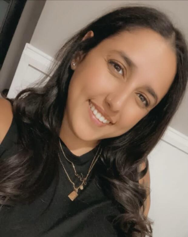 A woman with long brown hair wearing a black top and gold necklaces.