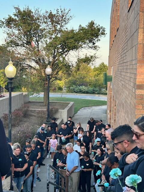 A large group of people wearing black clothing and holding teal carnations