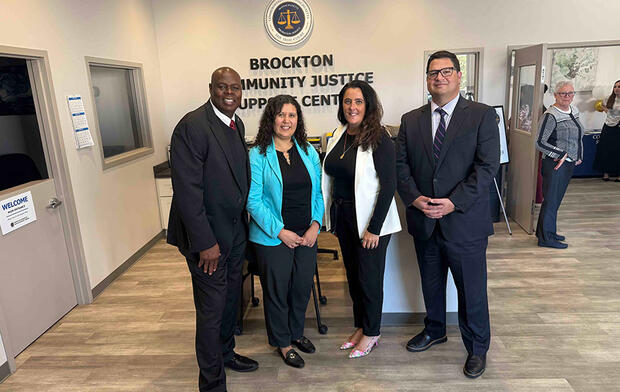 Four people standing in a community justice support center with a logo and text on the wall behind them.
