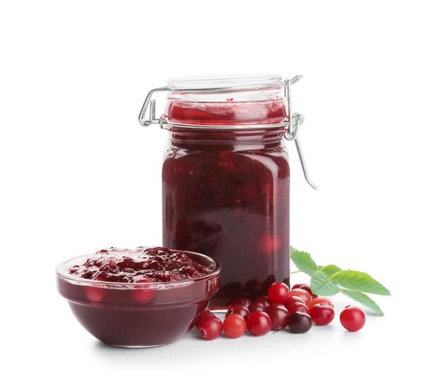 A mason jar and bowl of cranberry sauce next to a pile of fresh cranberries.