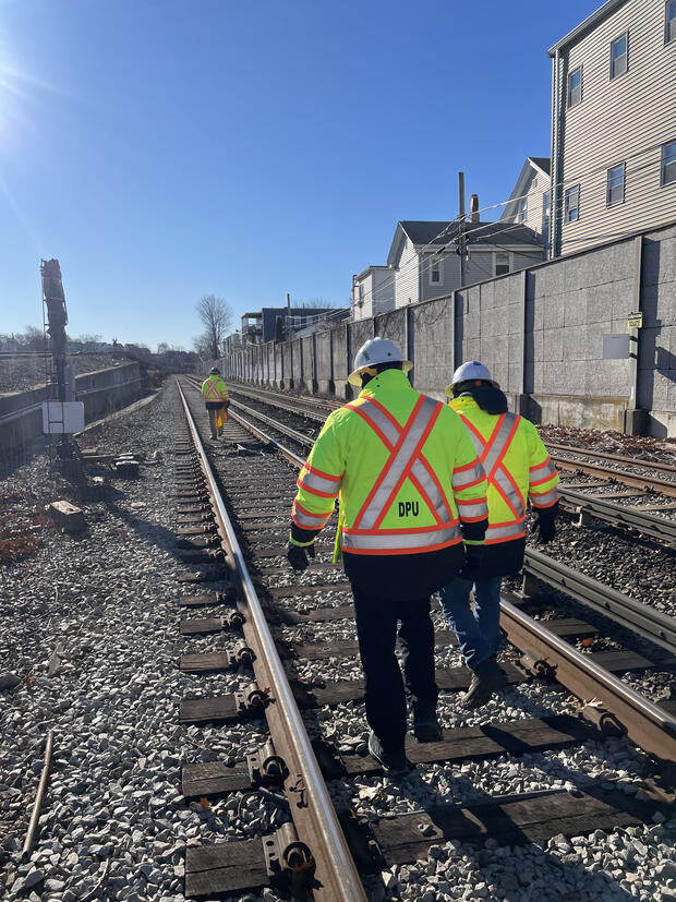 DPU and MBTA workers in safety vests walking and inspecting railroad tracks.