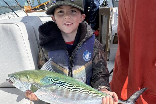 Man stands on boat with large bigeye tuna hanging above stern. 