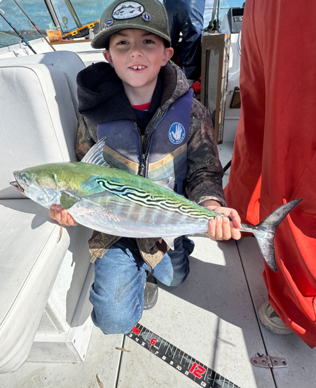 Young boy sits holding an albacore. 