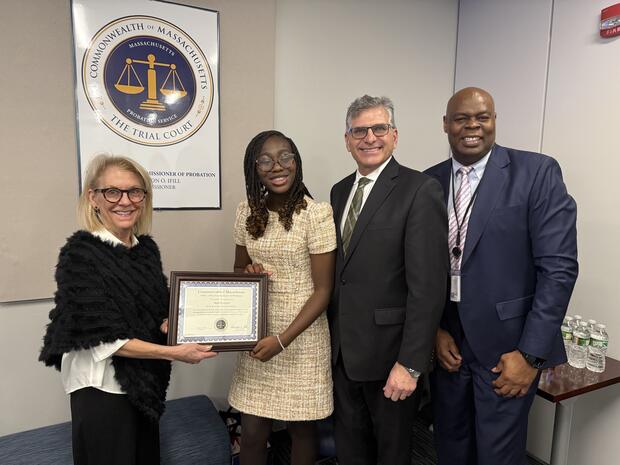 Four people in a conference room with the first two holding a certificate together.