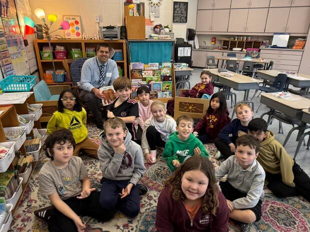 A man holding a children's book poses with a group of children