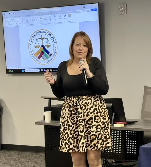 Julie Grady speaks to a crowd with an image of the Cultural Appreciation Week logo behind her