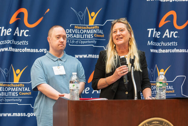 Sandra Heller and Craig Kinney speaking into a microphone at a podium.
