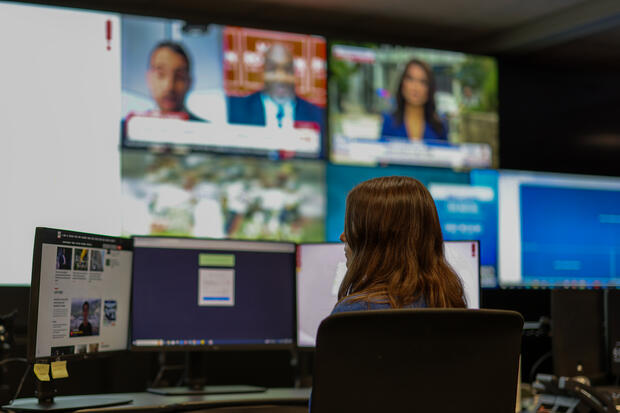 A young woman seated at a computer workstation, monitoring and tracking operations on multiple screens.