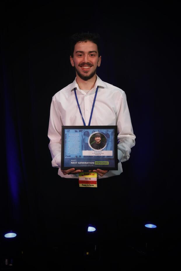 dark haired man standing with award certificate in his hands