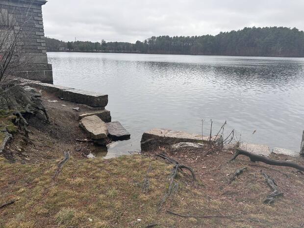 shore of northern basin of lake Cochituate with low masonry wall that has a break in it where a cartop boat can be launched