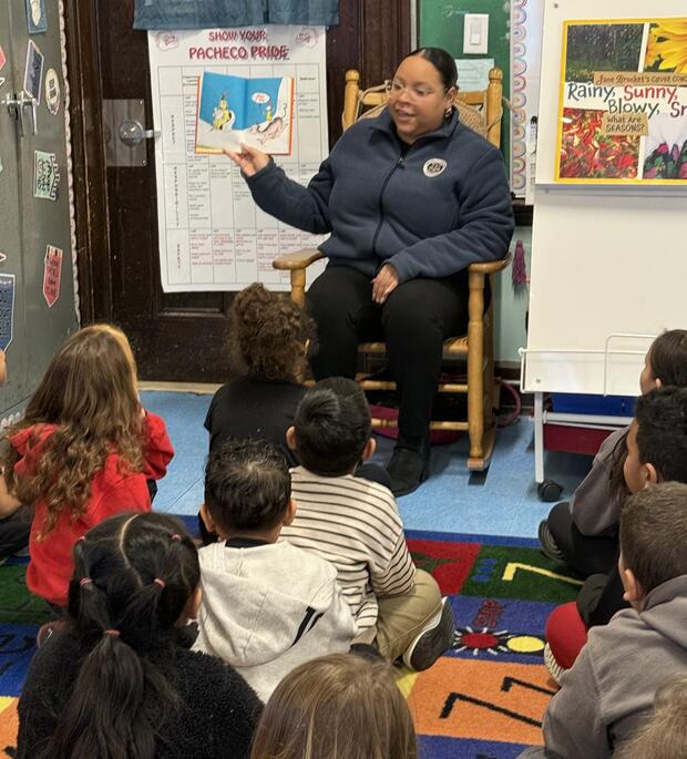 A person in a rocking chair reading a book to children.