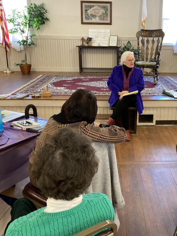 A woman sitting on the edge of a stage talking to a group of people.