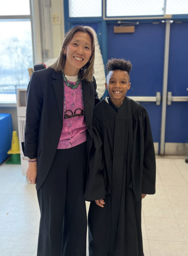 A woman stands with a student who is wearing a judge's robe.