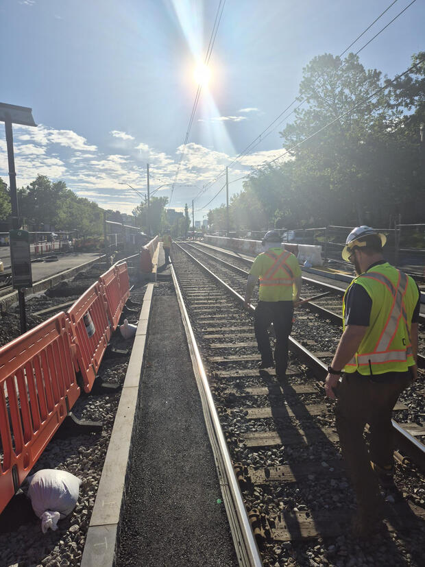 Two workers in reflective safety vests inspect the Green Line tracks.
