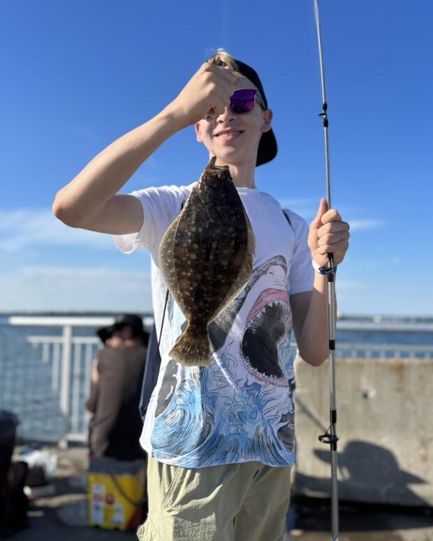 A young angler holds up a flatfish he just caught fishing from an ocean pier.