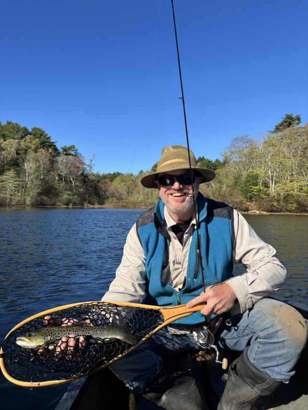 man holding fishing equipment with trout in a lake