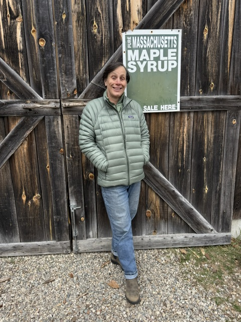 woman leaning on barn doors next to a maple syrup sign