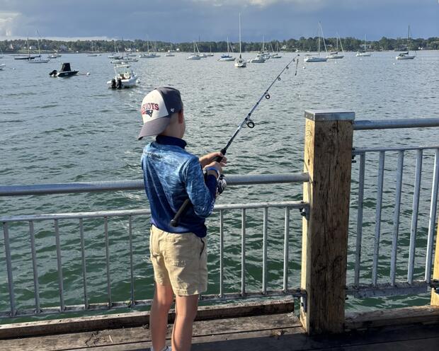 A boy fishing from an ocean pier.