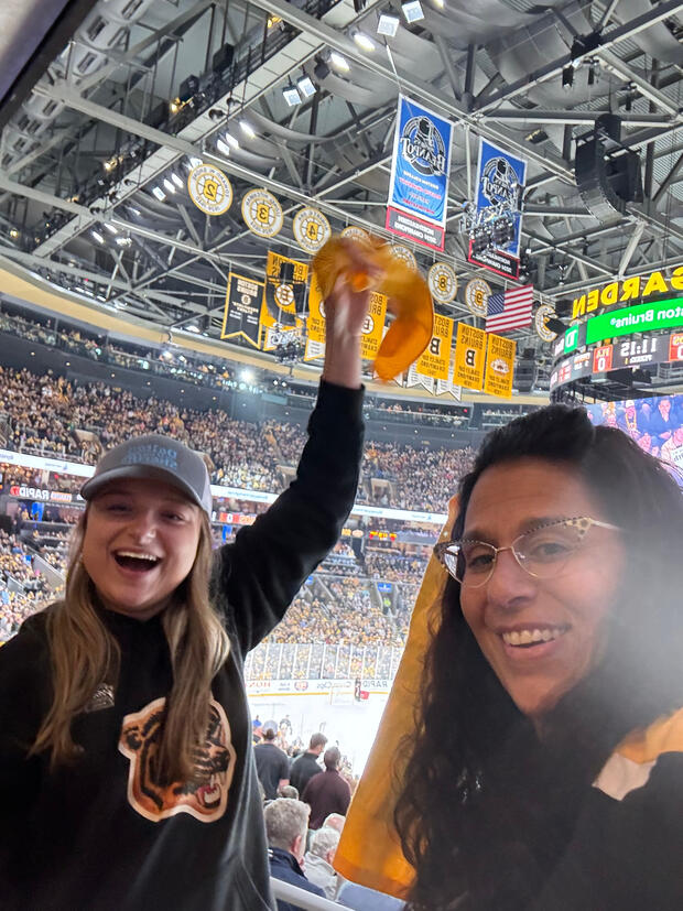 Selfie of Undersecretary D’Emilia and daughter smiling and cheering at a Boston Bruins game. A full stadium of fans is in the background. 
