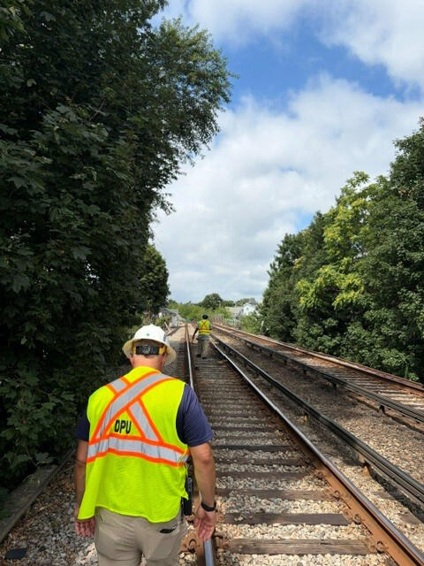 DPU engineer in a yellow and orange safety vest conducts a track inspection.