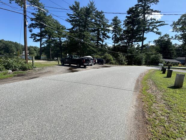 small gravel parking area with cars adjacent to narrow road bound by houses
