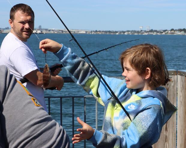 A kid with a rod holding a small fish they caught from an ocean pier.