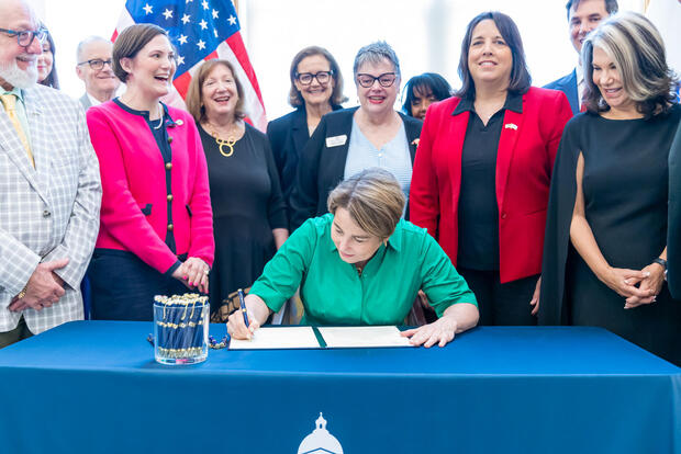 Governor Healey sits at a table and signs Executive Order 642