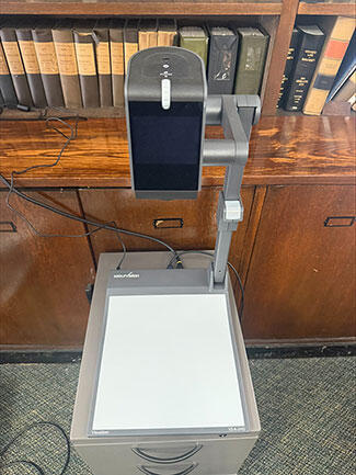 A WolfVision document camera stands in front of a wooden bookcase filled with law books.