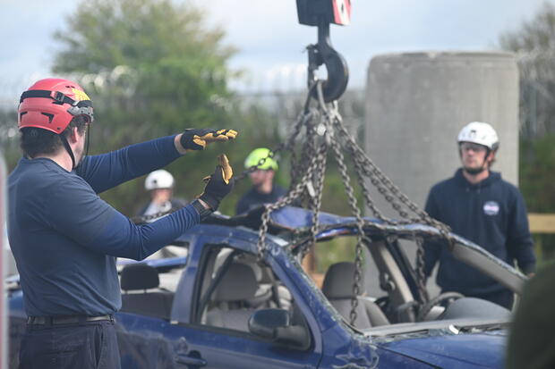 Firefighter using hand signals near a vehicle loaded onto a crane